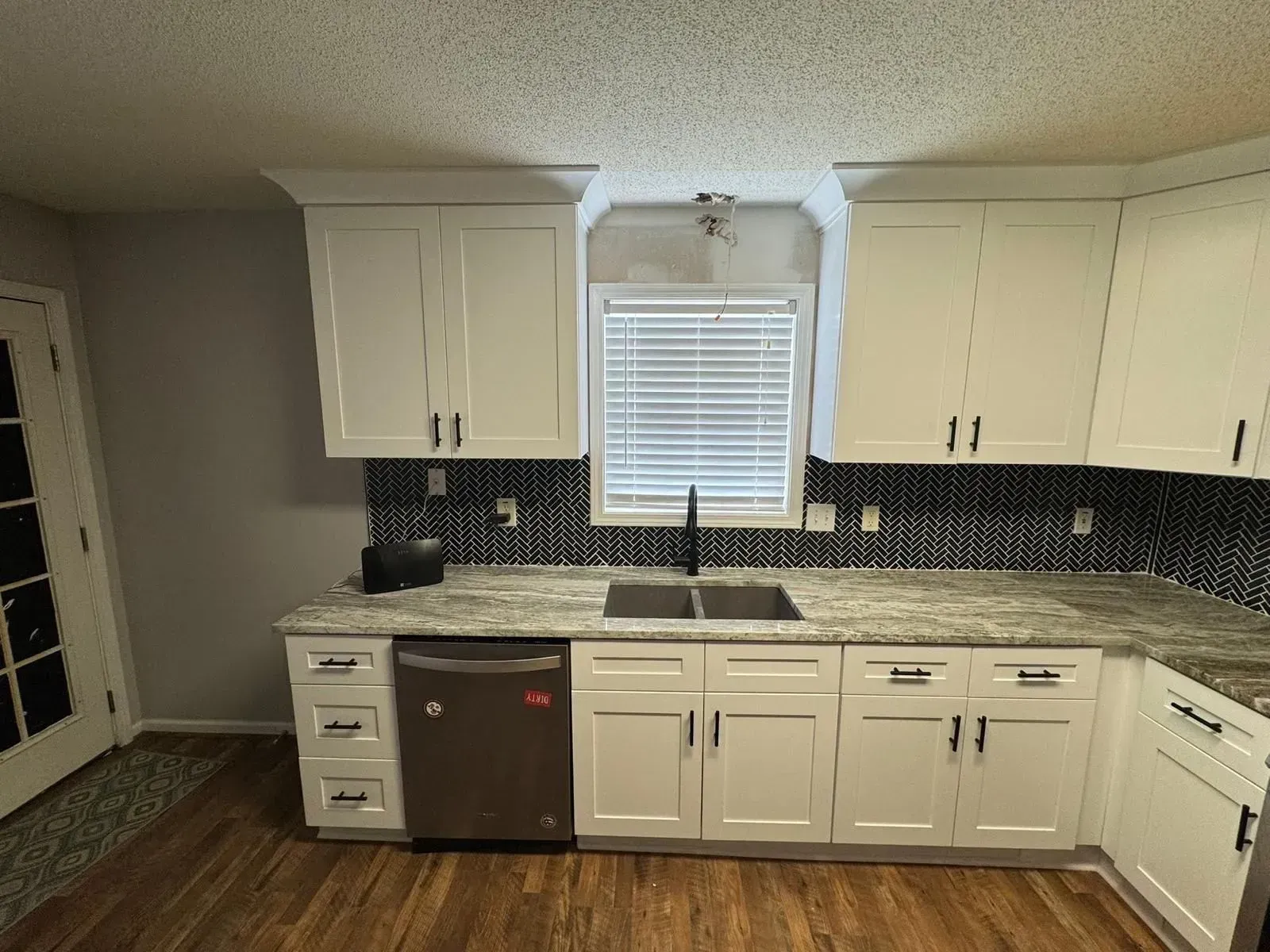 White kitchen cabinets, stainless steel appliances, granite countertops, and black backsplash.