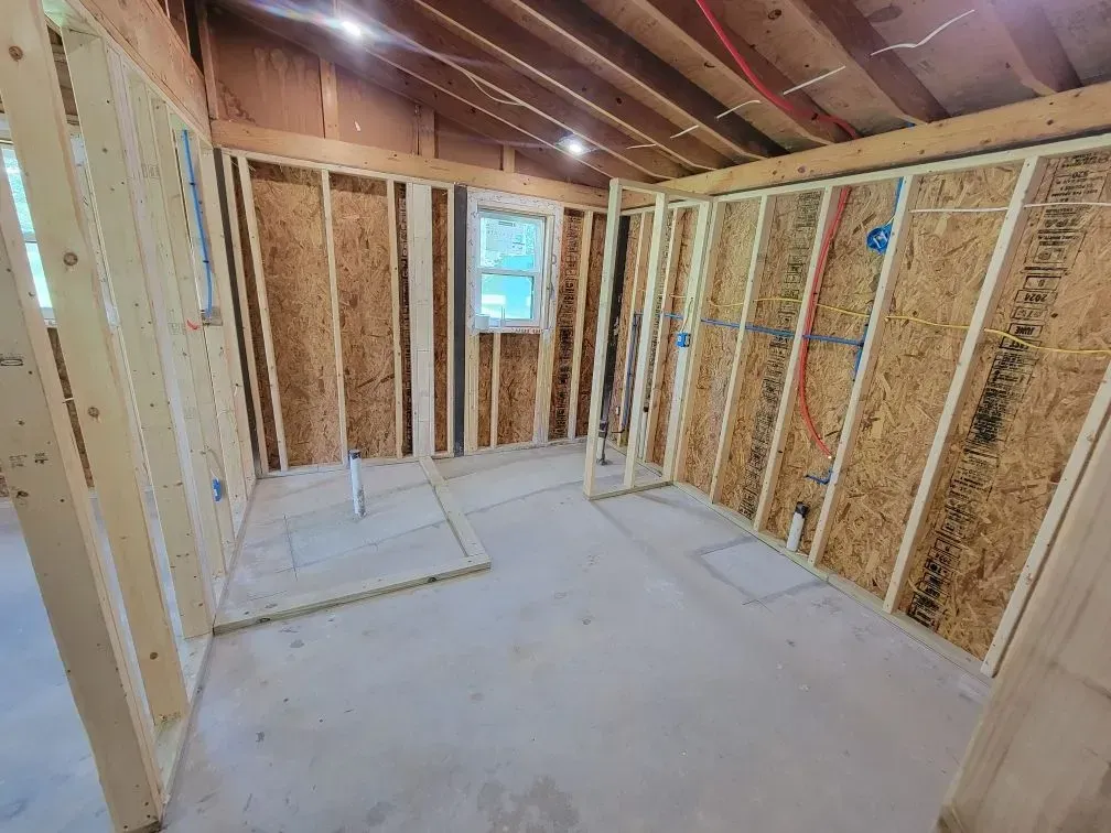 Interior framing of a room under construction with exposed wood studs, plumbing, and electrical.