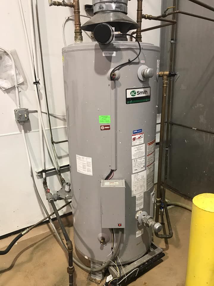 A gray water heater is sitting in a room next to a yellow pole.