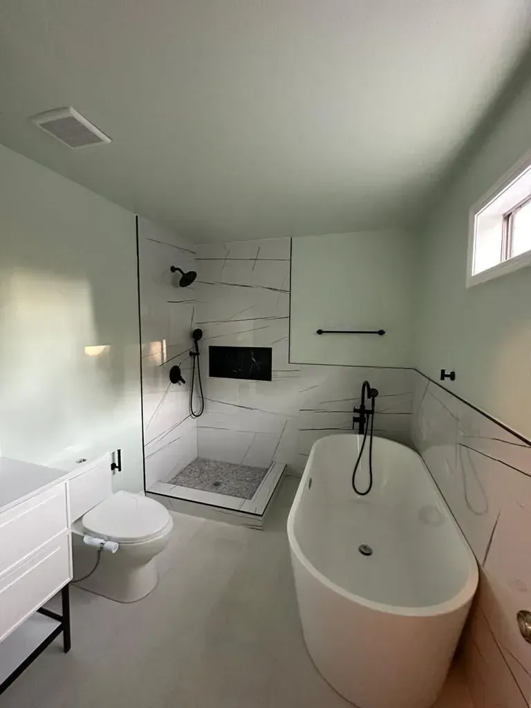 Modern bathroom with white tub, shower, and toilet. White and black tile accent wall, light green walls.