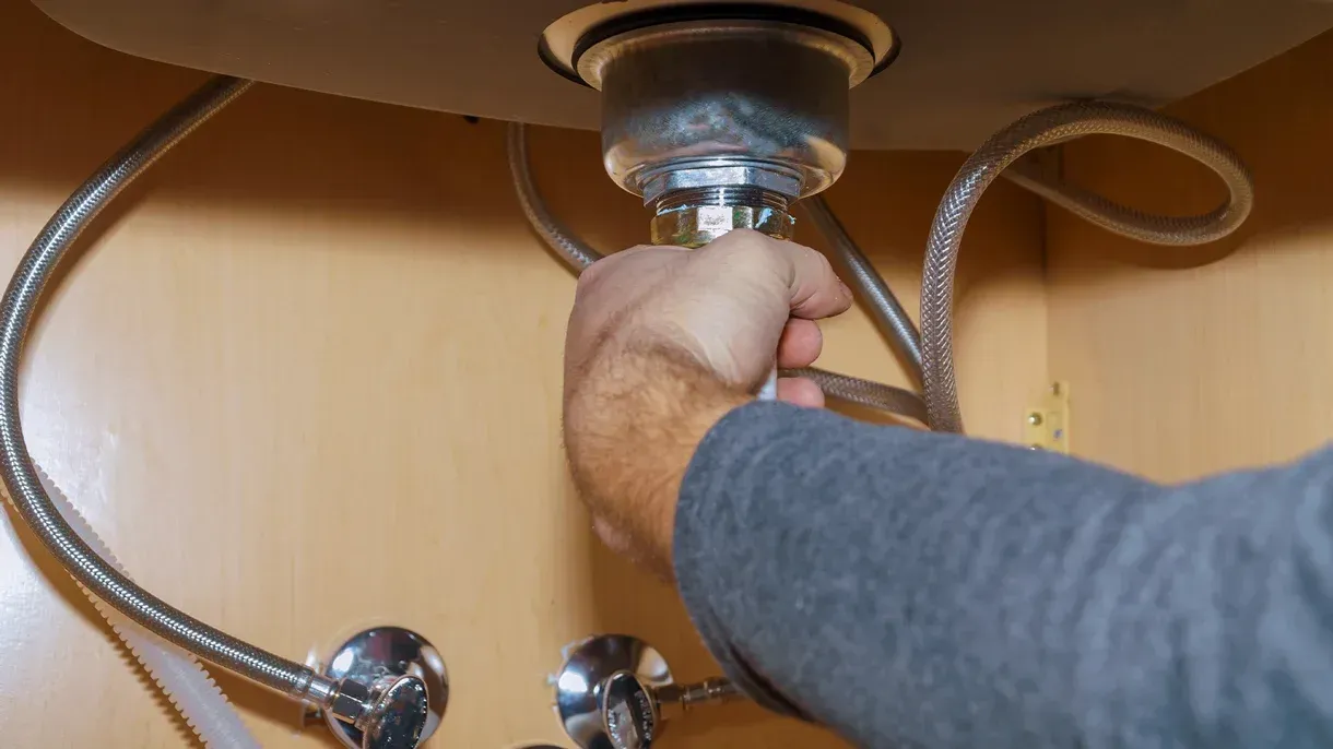 A man is fixing a sink with a wrench.