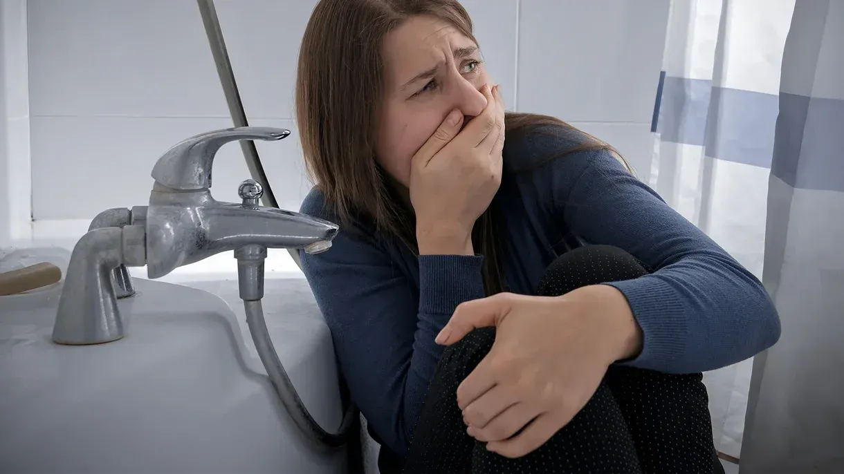 A woman is sitting in a bathroom covering her mouth with her hand.