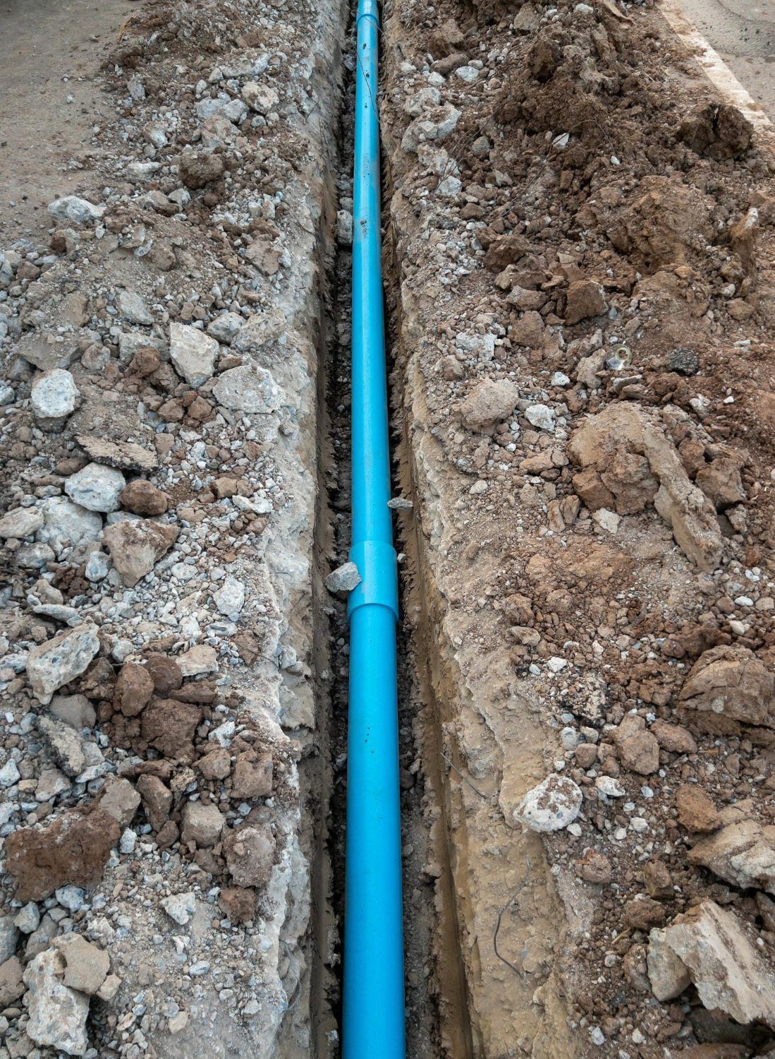A blue pipe is being installed in the dirt.