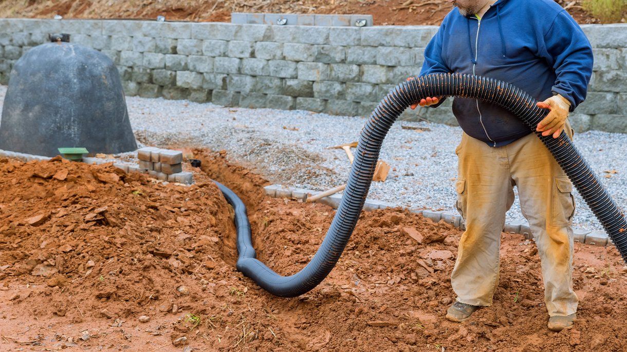 A man is standing in the dirt holding a large hose.