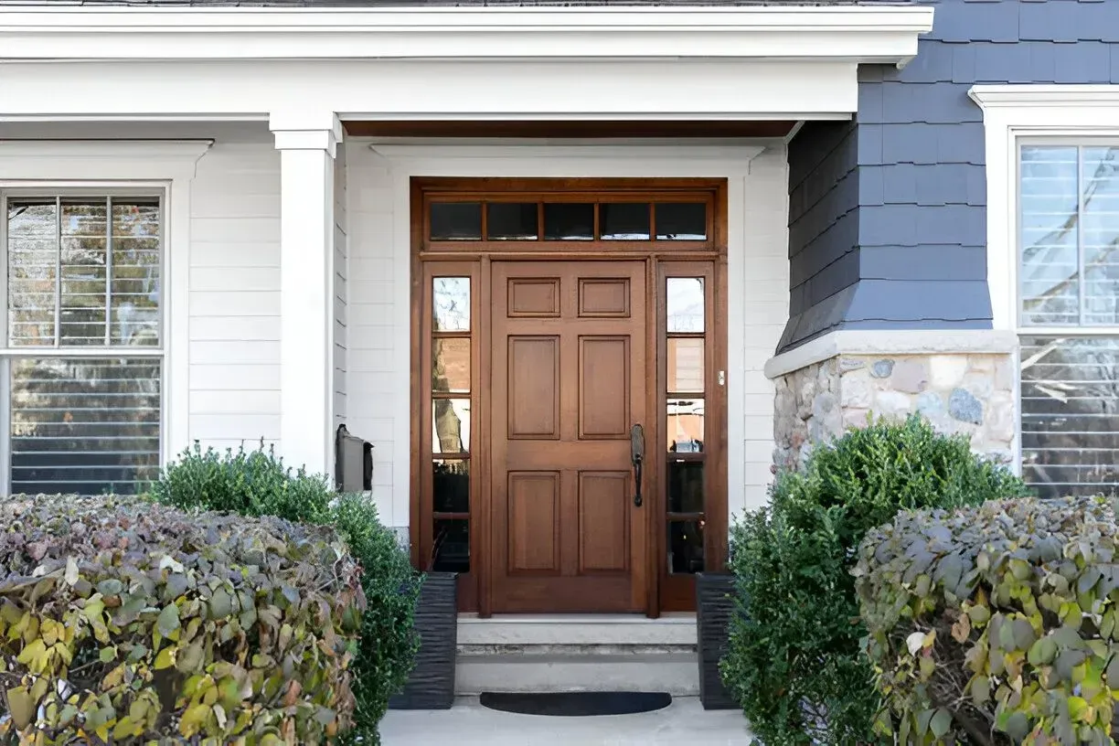 Brown wooden front door with sidelights, white trim, and a small entry step.