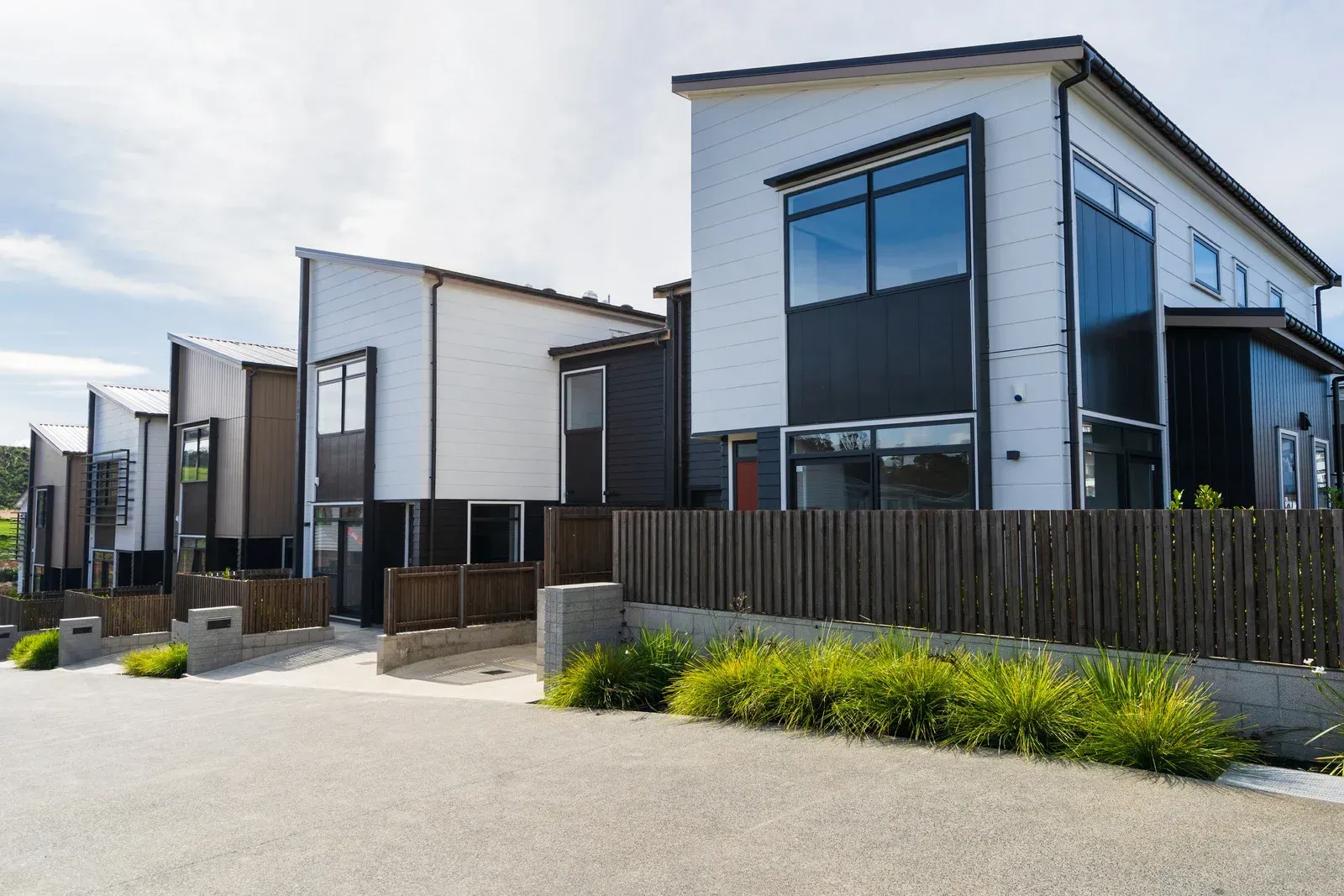 Modern townhouses with black and white exteriors, a low wooden fence, and green shrubbery.