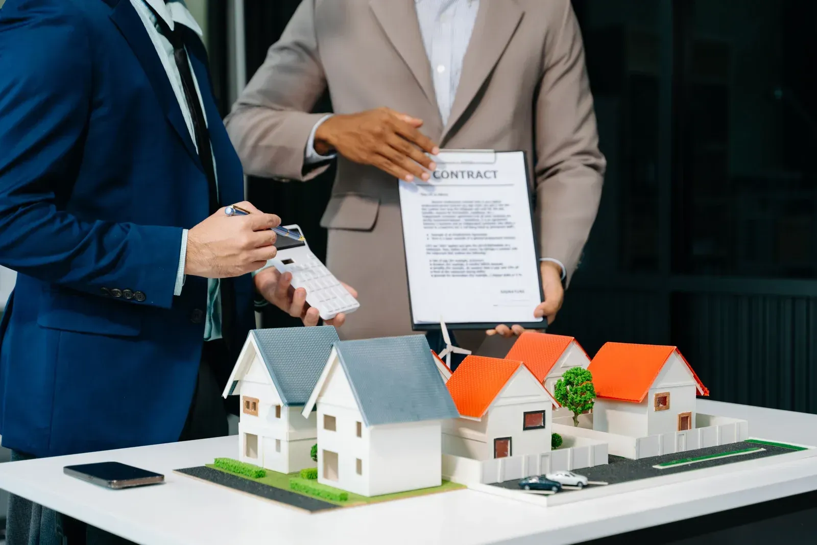 Two people reviewing a contract, with miniature houses on a table.