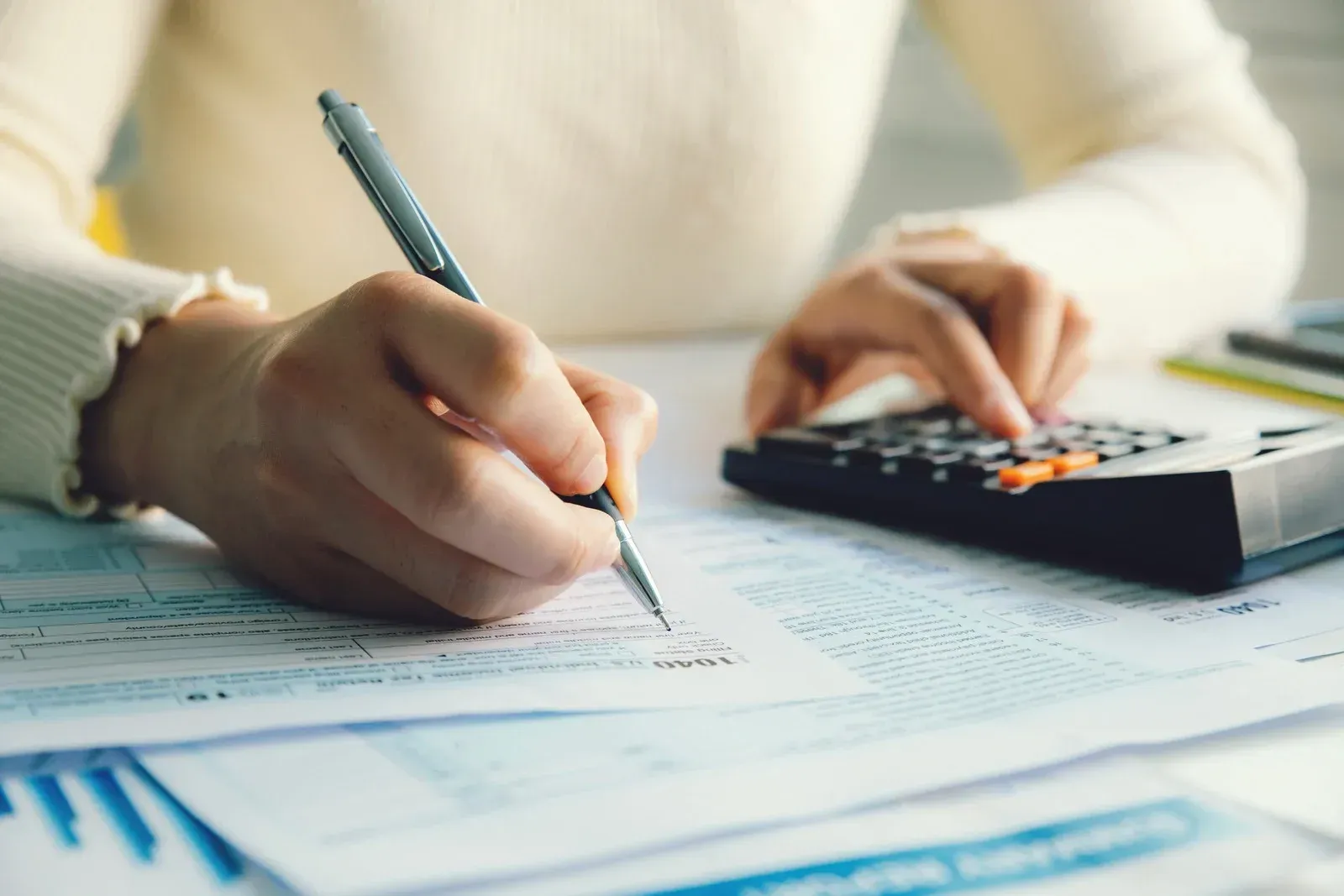 Person calculating taxes, using a calculator and writing on forms.