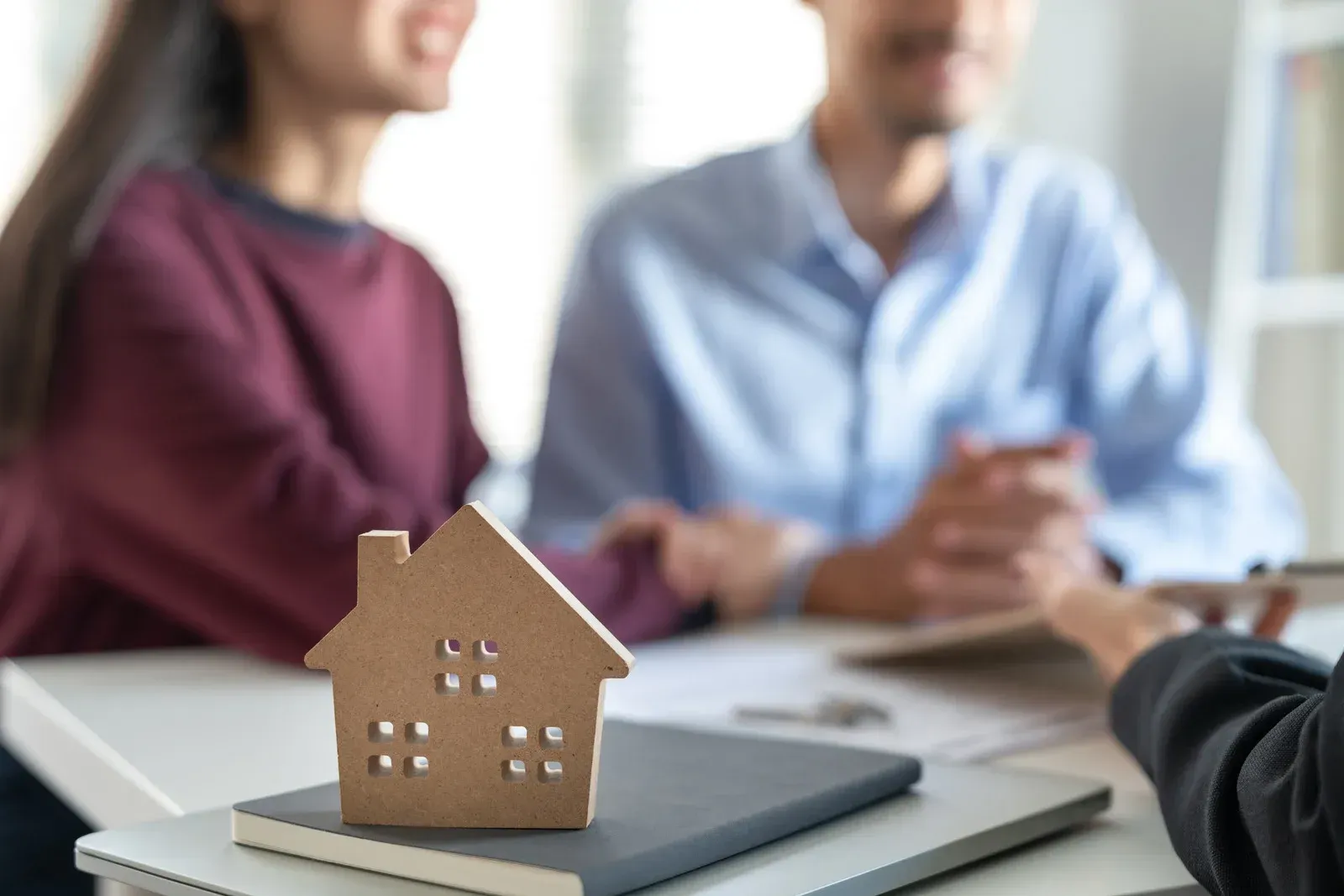 Couple with realtor, house cutout, and documents on a desk, likely discussing a home purchase.