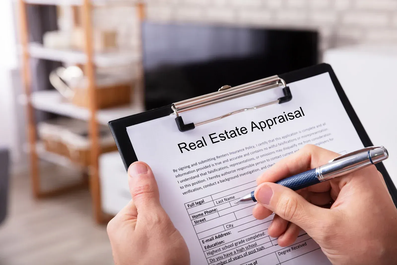 Person filling out a real estate appraisal form, with a TV and shelves in the background.
