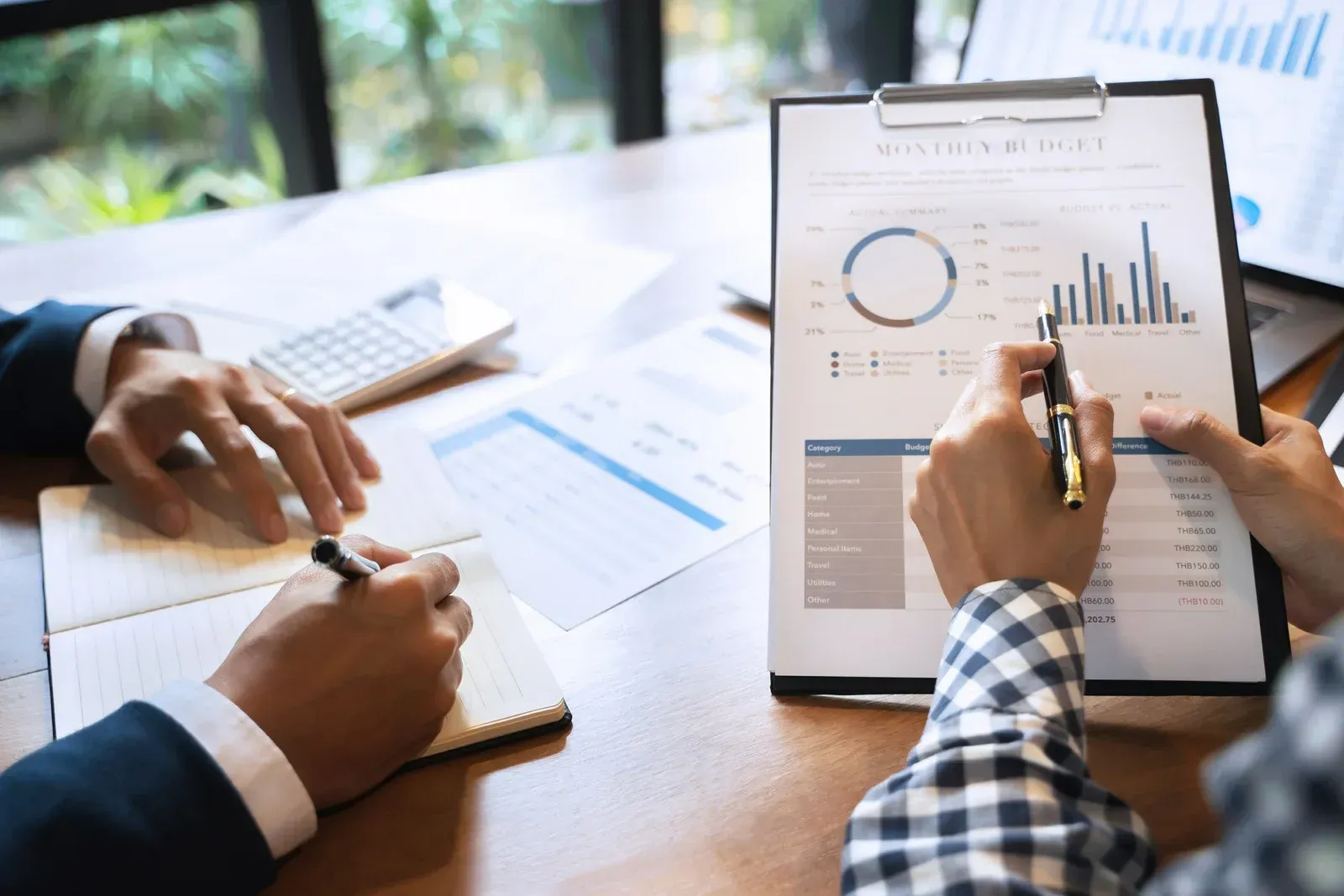 Two people reviewing financial reports at a table; one points to a chart, the other takes notes.