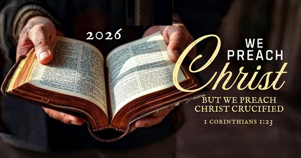 Hands hold an open Bible with text reading: "2026 WE PREACH Christ BUT WE PREACH CHRIST CRUCIFIED 1 CORINTHIANS 1:23."