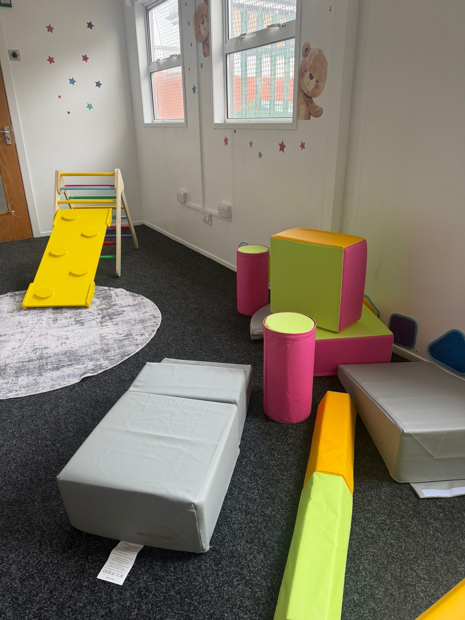 A playroom featuring a yellow slide and various foam climbing blocks in bright colors on a dark carpeted floor.