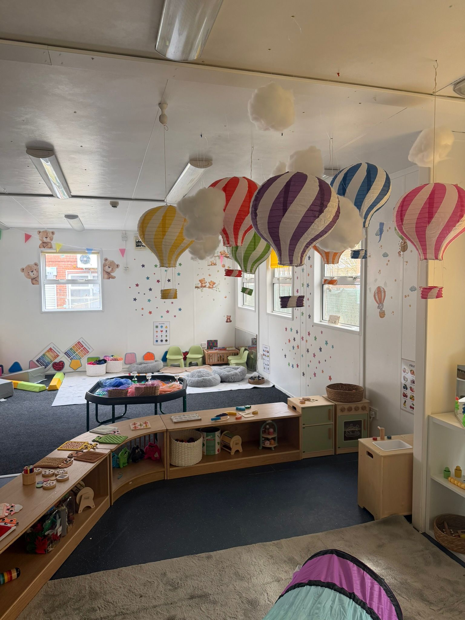 A colorful nursery classroom featuring several decorative hot air balloons suspended from the ceiling.