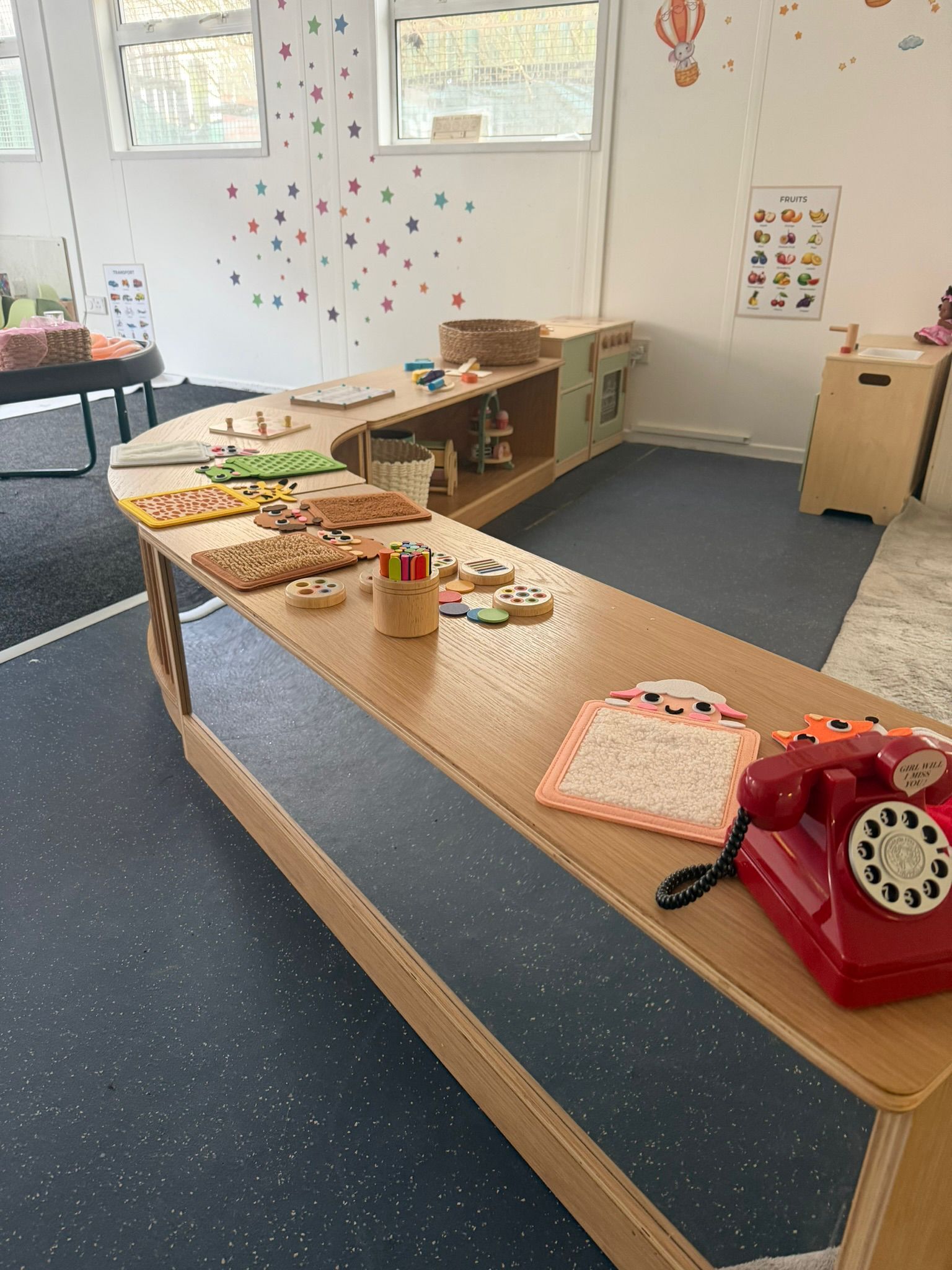 A wooden preschool activity table holding various toys, including a red rotary telephone, puzzles, and counting blocks.