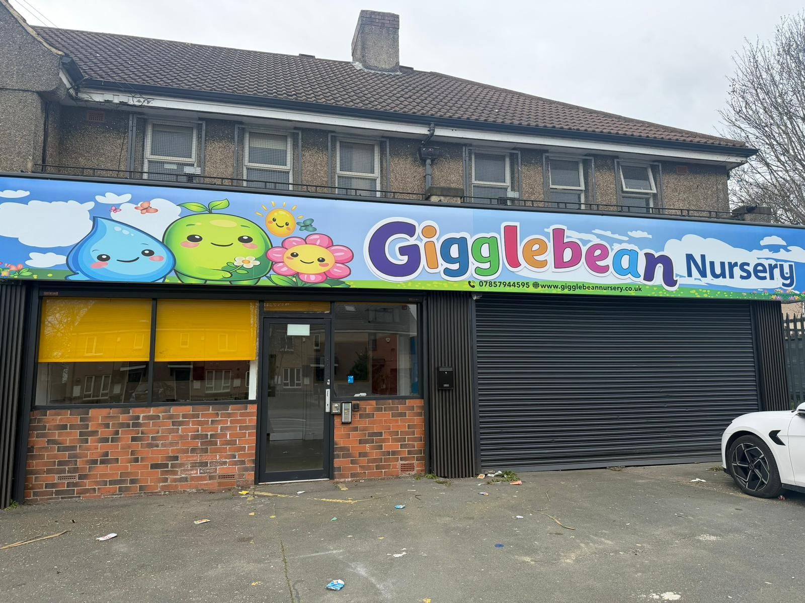 A storefront for Gigglebean Nursery featuring a colorful sign with cartoon characters above a brick and glass entrance.
