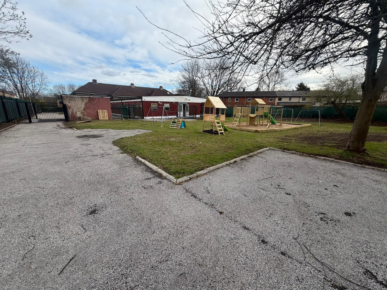 A spacious backyard features a gray gravel driveway leading to a lawn with a wooden play structure and a small white house.