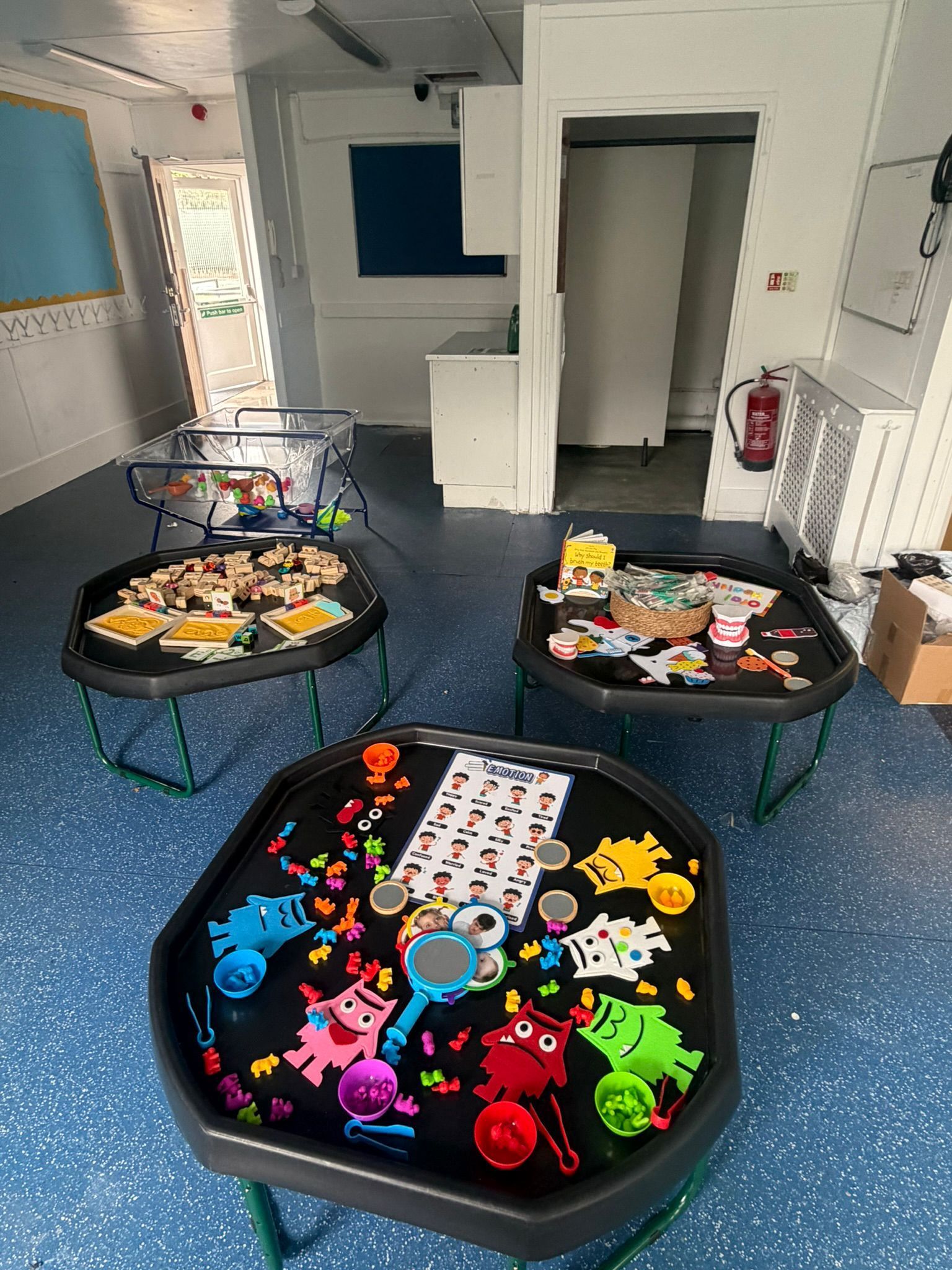 Three hexagonal activity trays with colorful toys and learning materials arranged in a classroom with a blue floor.