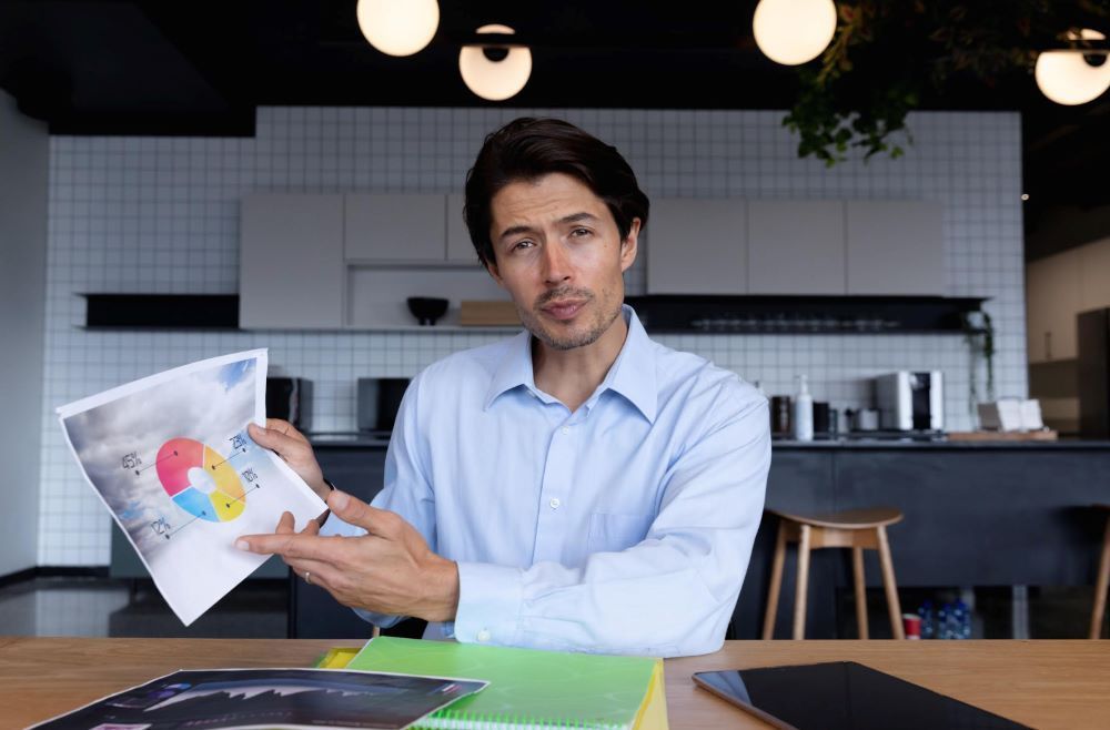 Um homem está sentado à mesa segurando um pedaço de papel com um gráfico.