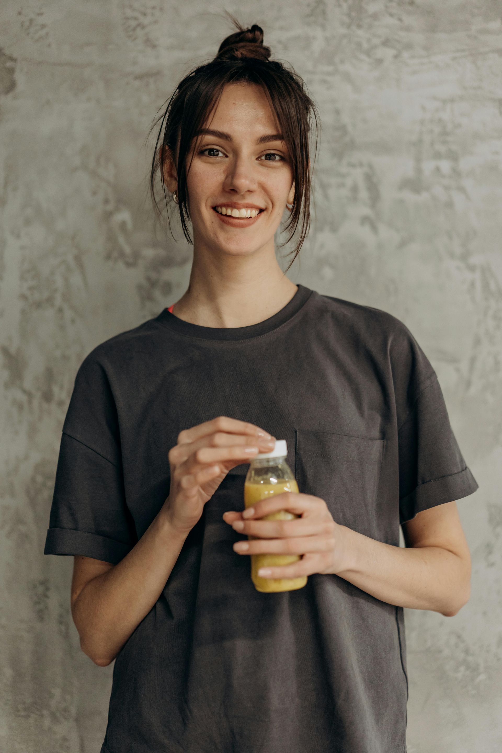 Woman with dark hair in a bun, smiling and holding a bottle of yellow liquid. 