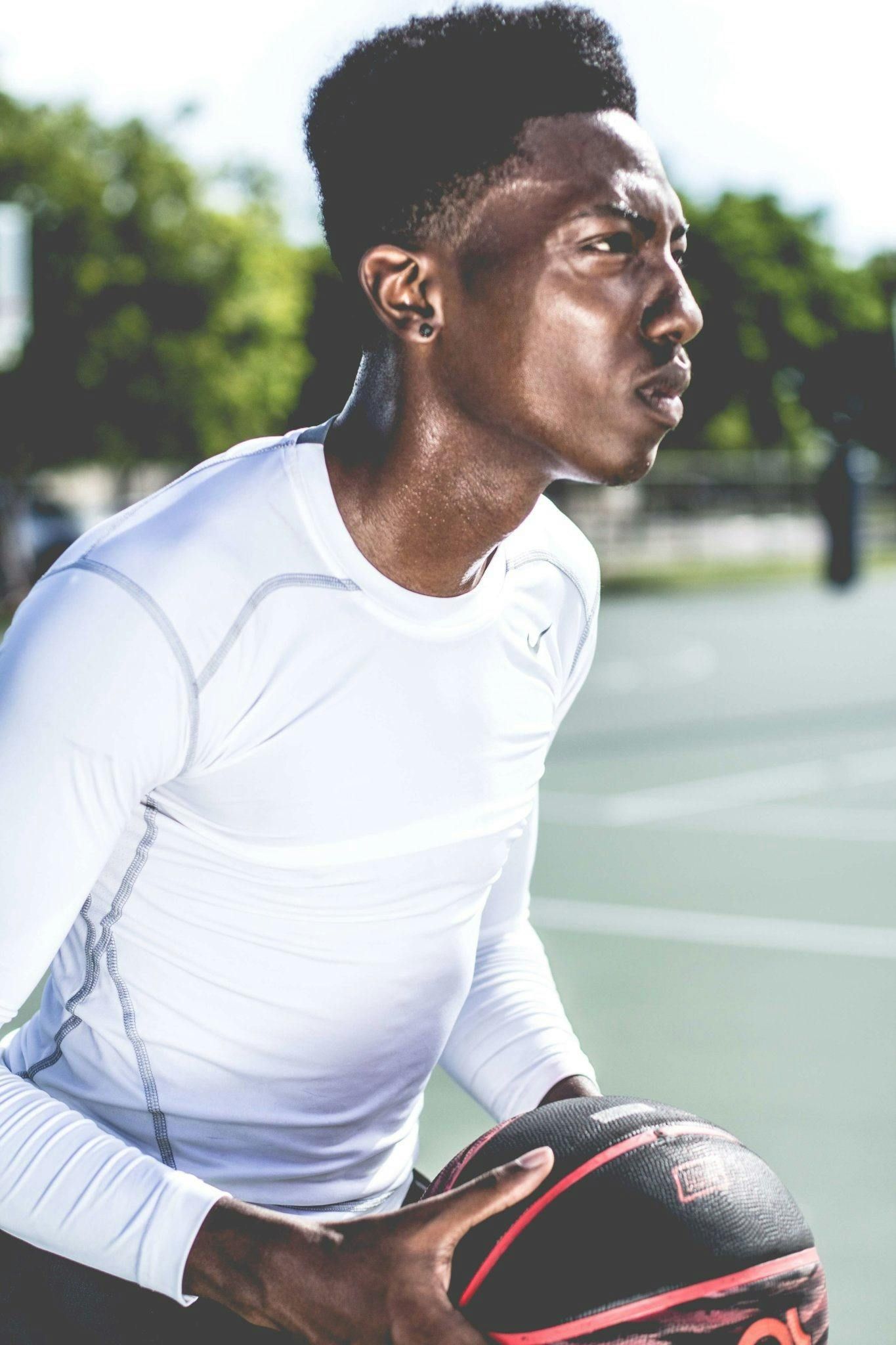 Man in white athletic wear, sweating, holding a basketball on a court, focused gaze.