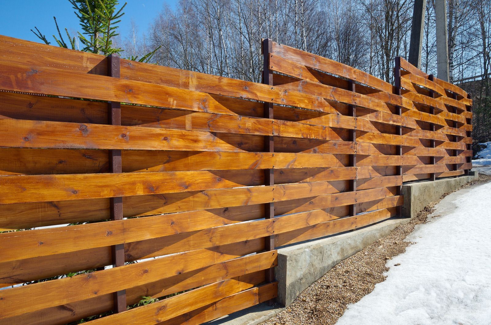 A wooden fence is sitting on the side of a snowy road.