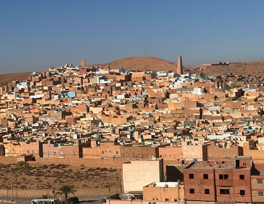 A densely packed desert town in Algeria, featuring traditional mud-brick houses and a minaret against a clear blue sky.