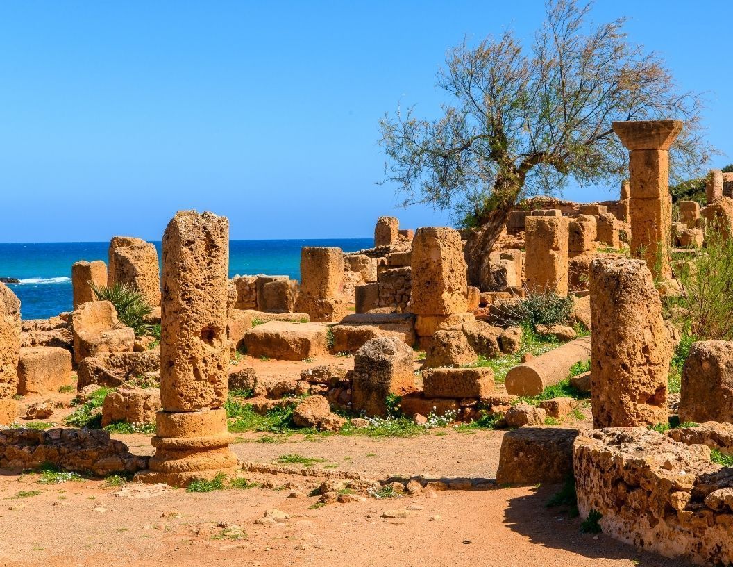 Ancient stone ruins with weathered columns overlooking a blue sea under a clear sky.