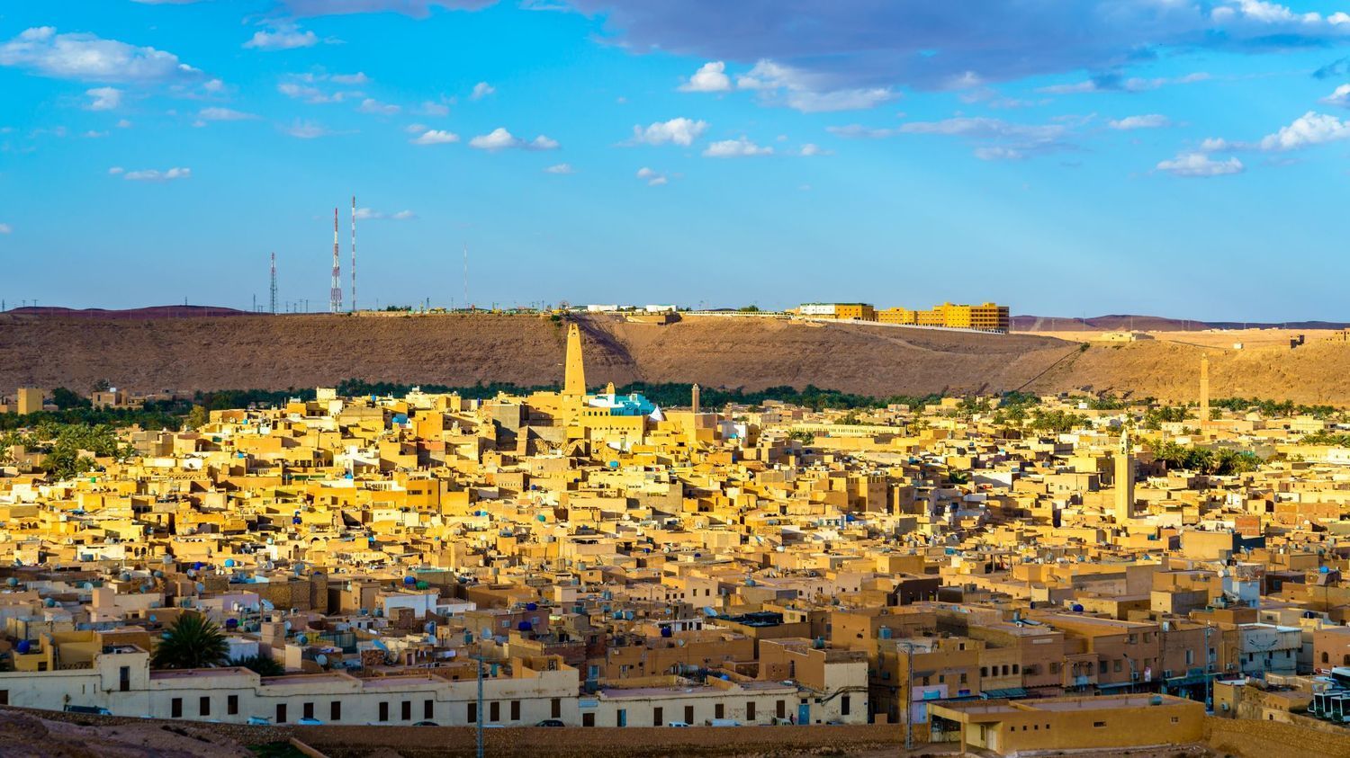 A golden-toned town with historic earthen architecture and prominent minarets nestled beneath a desert plateau.
