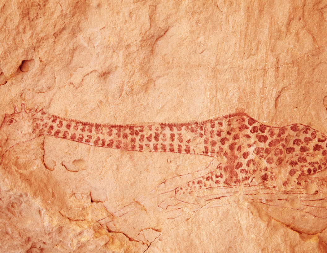 A red, spotted rock art painting of a giraffe silhouette against a textured, light-colored stone surface.