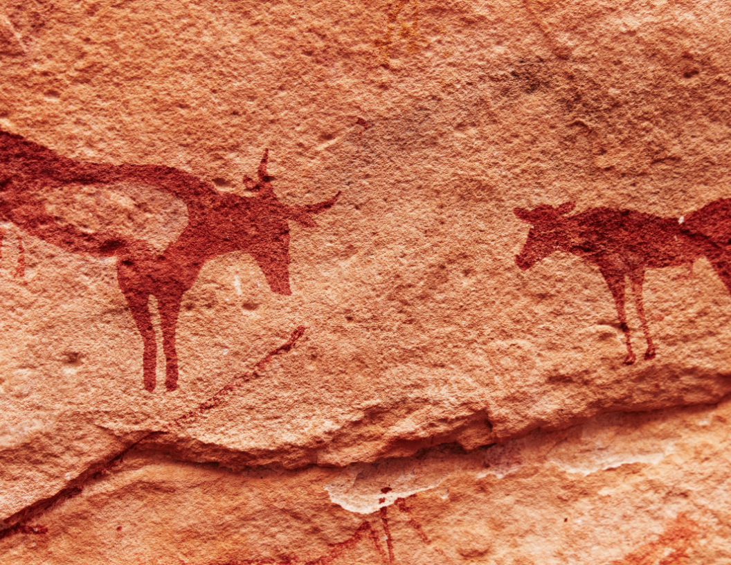 Red ochre petroglyphs of two horned animals painted on a textured, light brown rock surface.