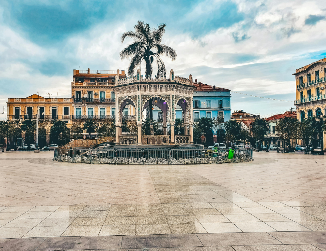 A historic, ornate gazebo stands in the center of a wide stone plaza, surrounded by colorful multi-story buildings.