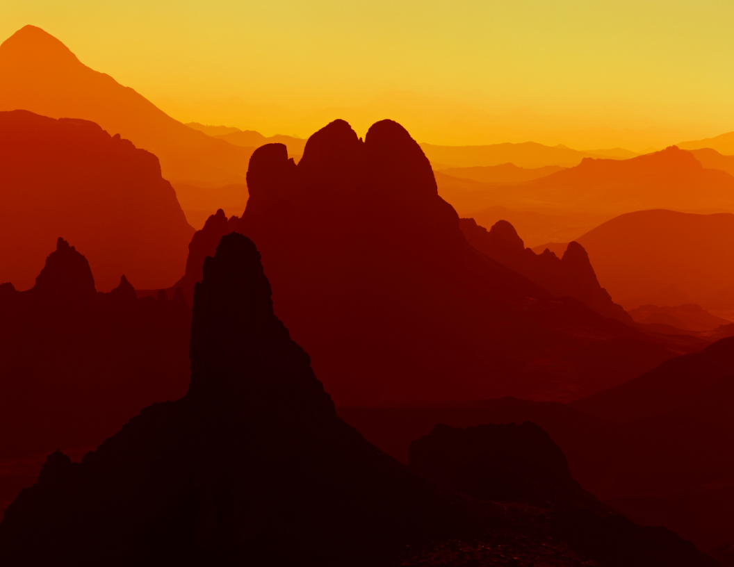 Silhouetted mountain peaks against a vibrant orange and yellow gradient sunset sky.