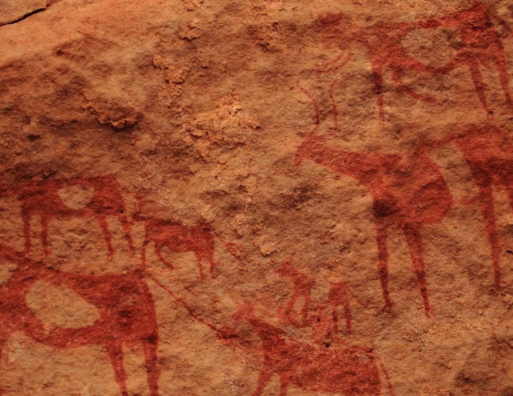 Red-pigmented rock art depicting stylized cattle and human figures on a textured sandstone surface.