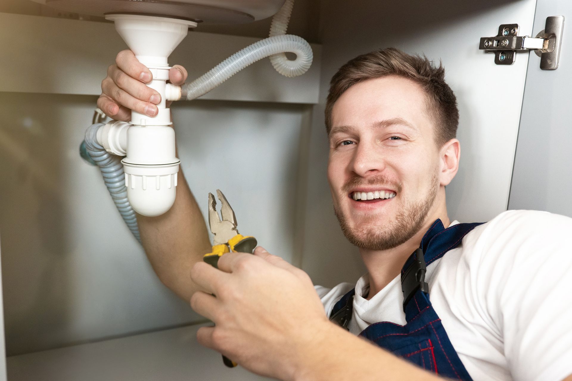 Smiling male plumber fixing the sink with pliers in his hand.