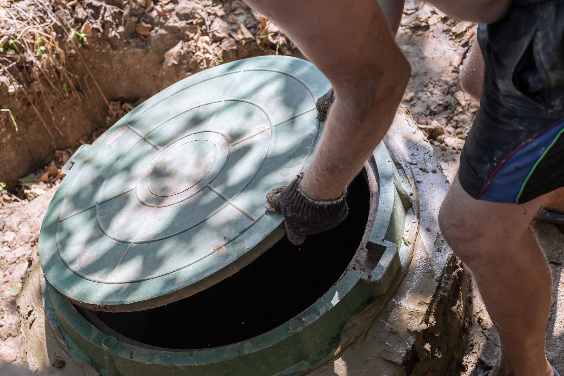 Person lifting the lid of a green septic tank in an outdoor setting.