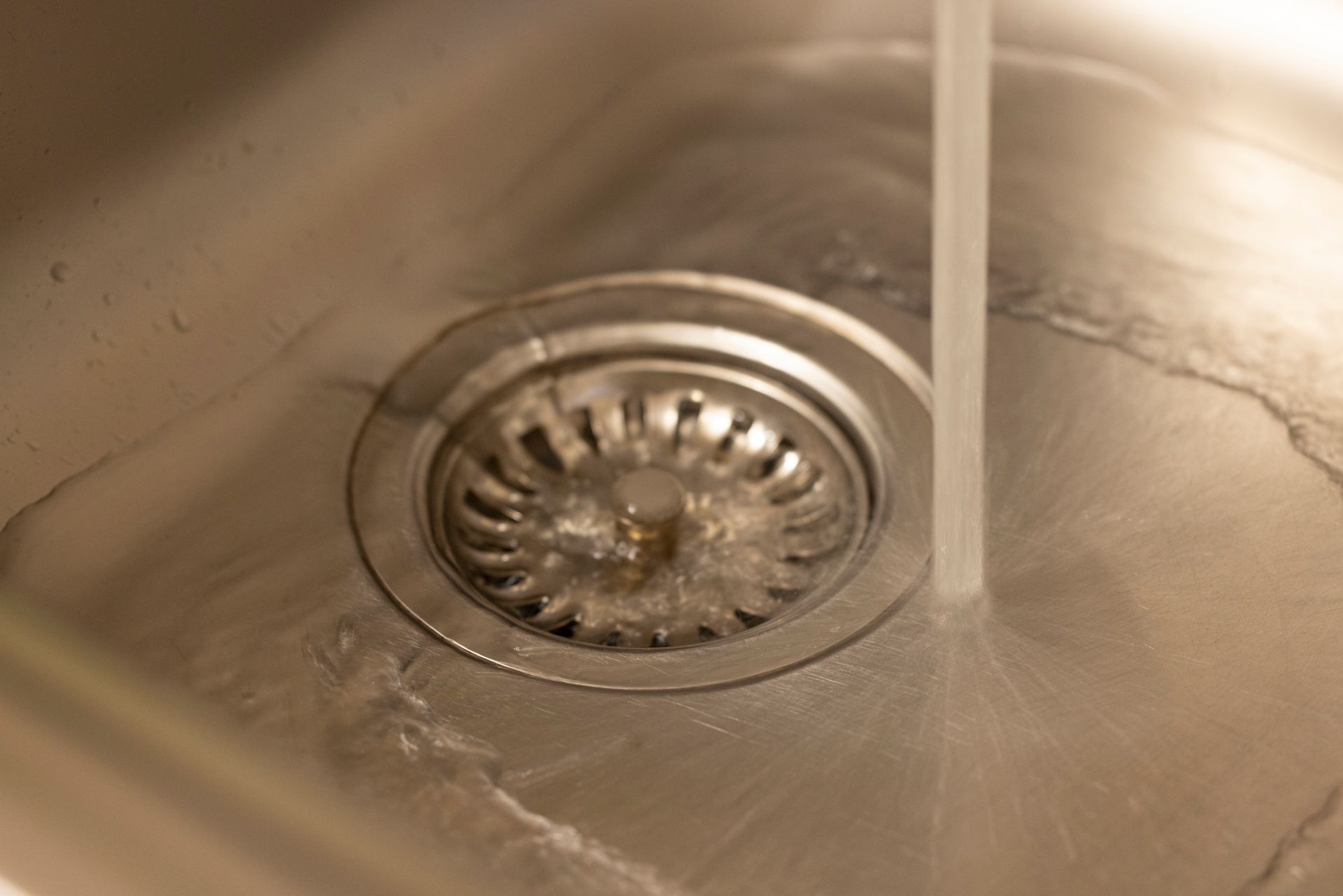 Close-up of water flowing into a stainless steel sink drain.