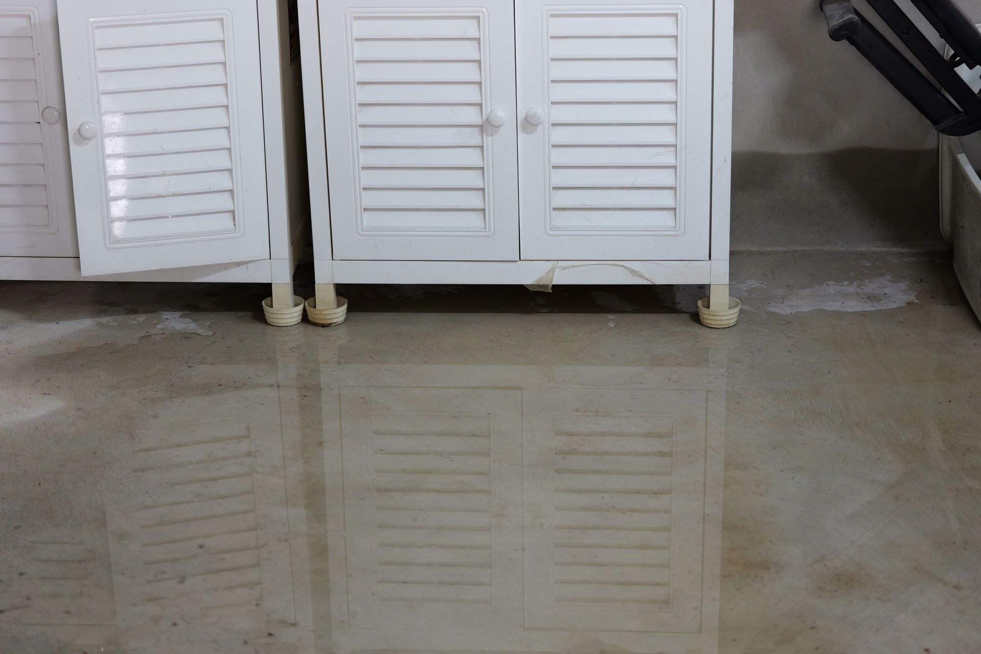 A white slatted cabinet stands on a floor with standing water, creating a clear reflection of the furniture.