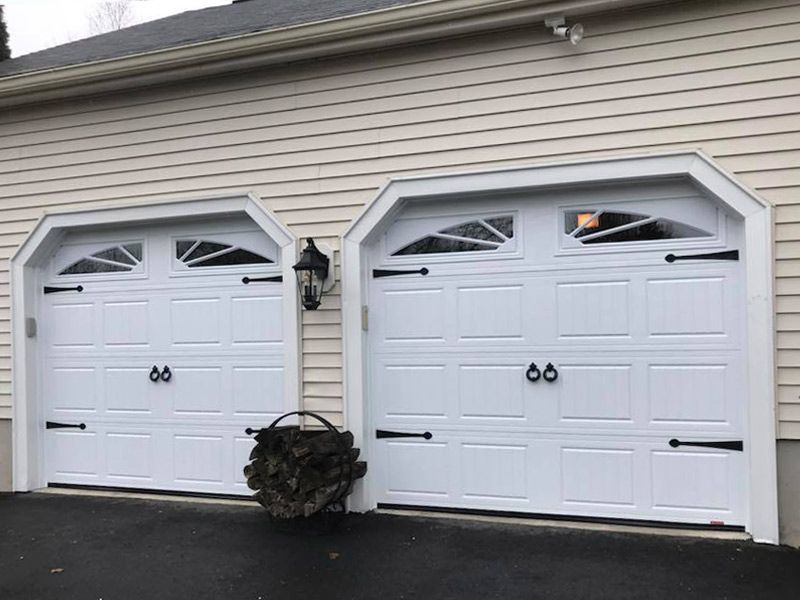 Two white garage doors are sitting next to each other on the side of a house.