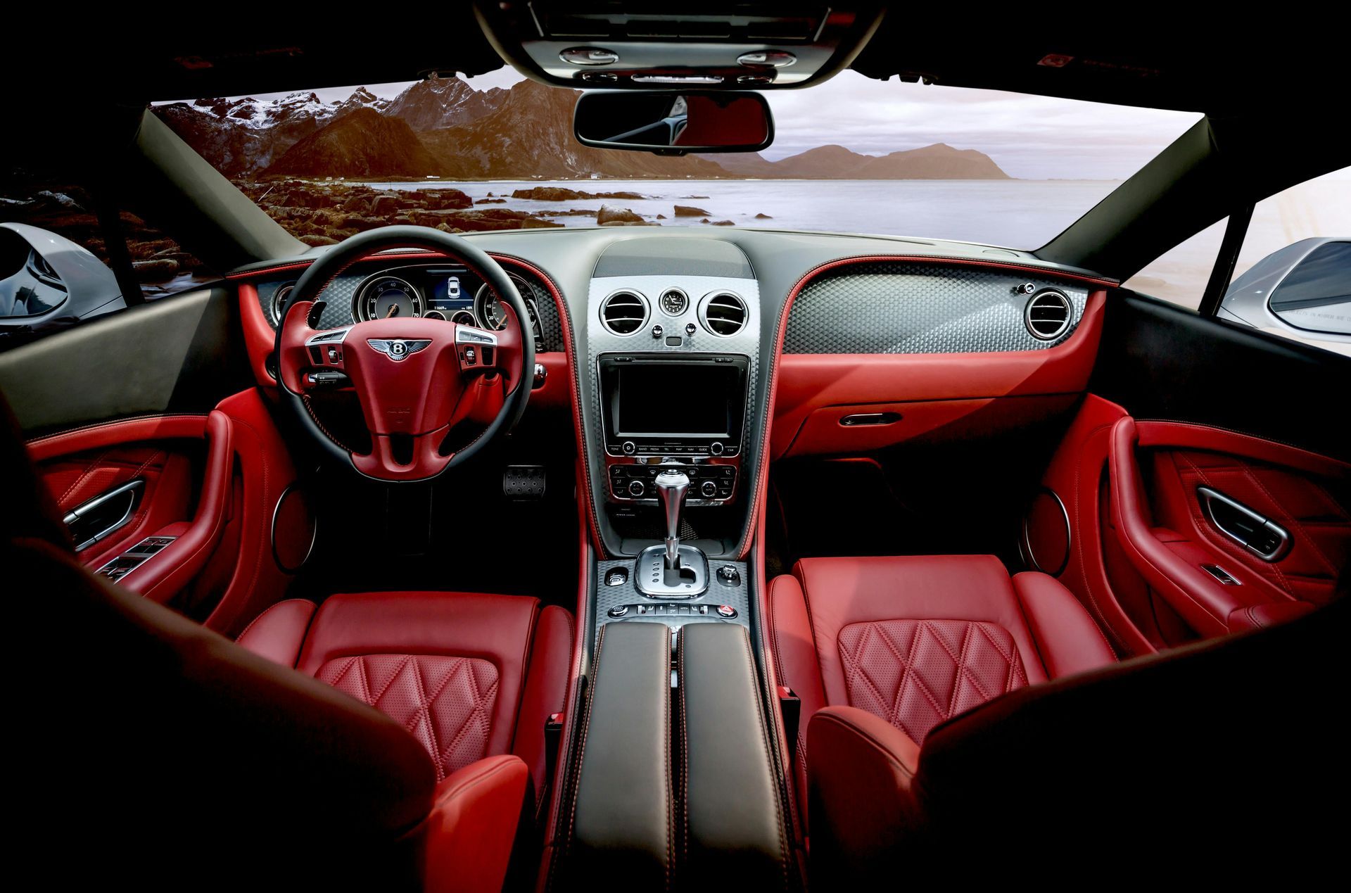 Interior view of a red Bentley car with a leather interior, dashboard, and a view of the ocean through the windshield.