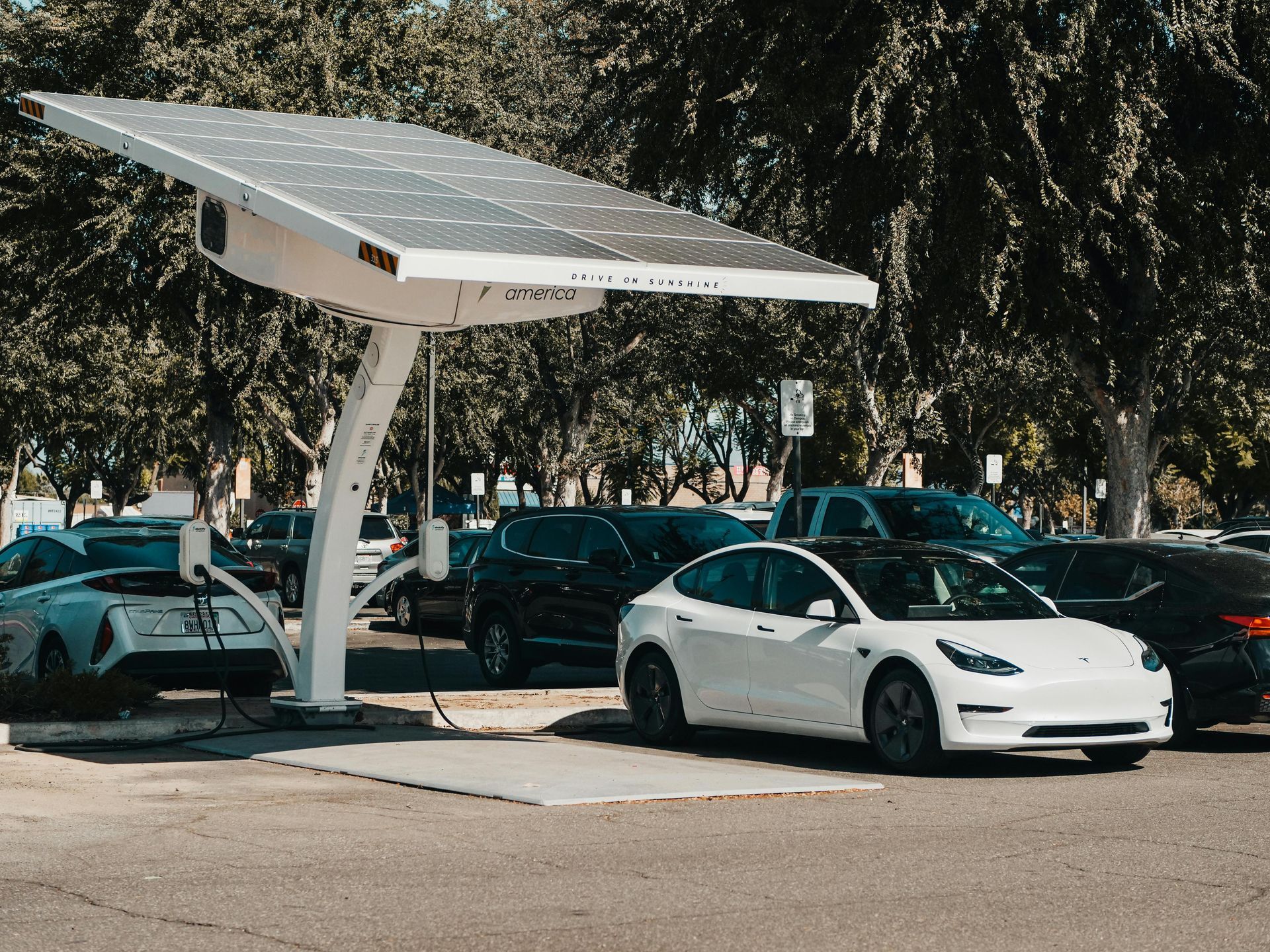 Solar panel canopy over EV charging stations in a parking lot; white Tesla charging.