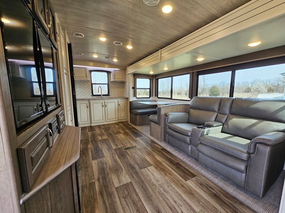 Interior of a camper with hardwood floors, kitchen, seating area, and large windows.