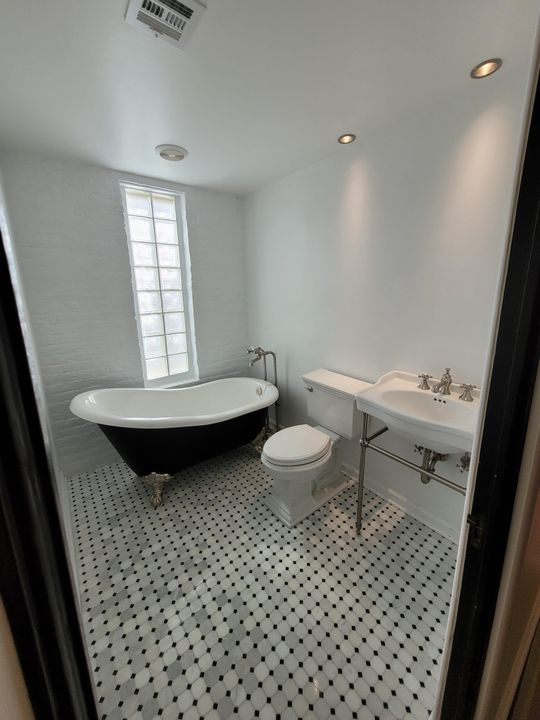 A bathroom with a tub , toilet , sink and window.