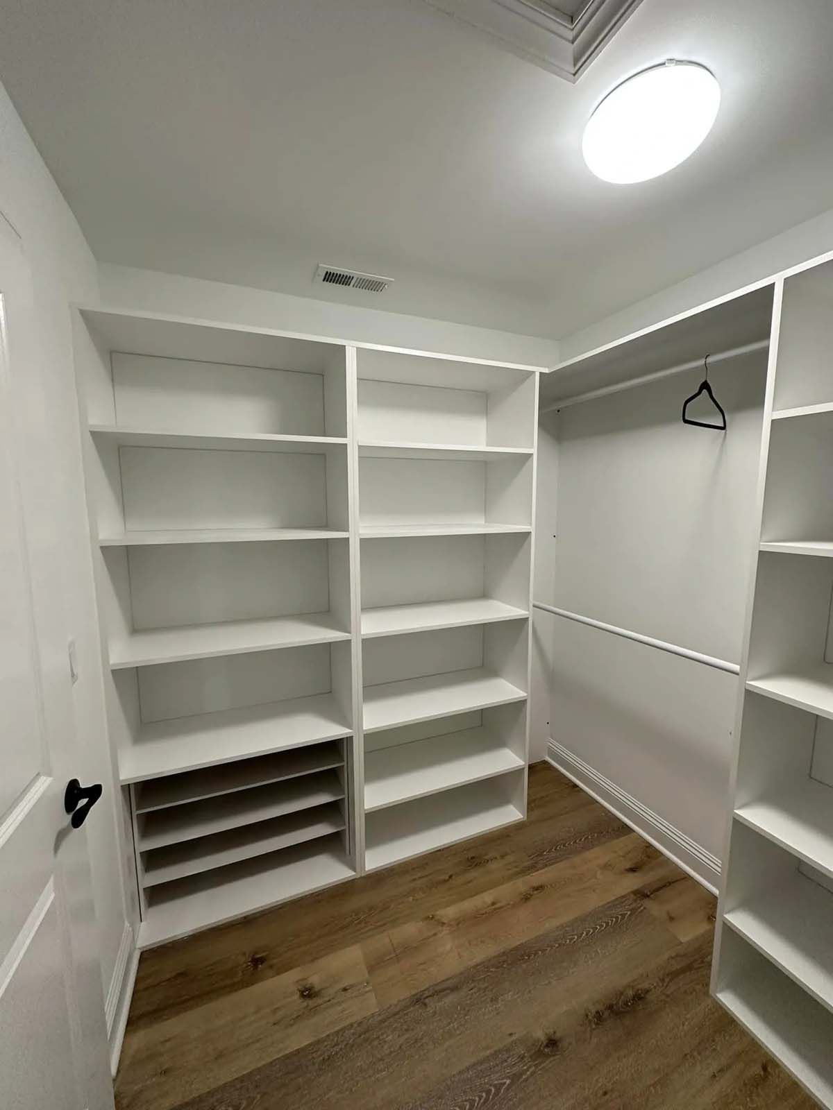 A walk in closet with white shelves and wooden floors.