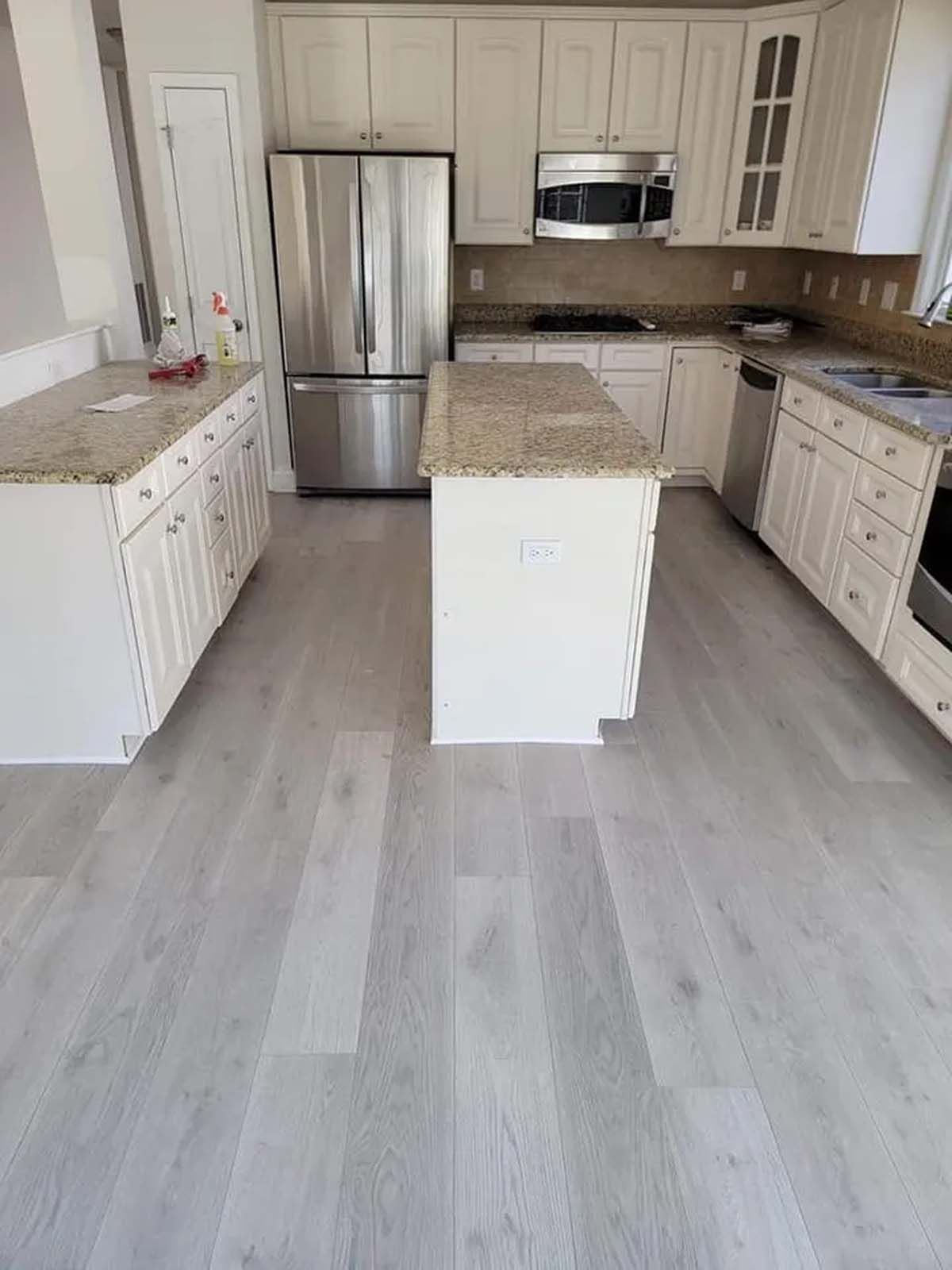 A kitchen with white cabinets , stainless steel appliances , granite counter tops and a large island.