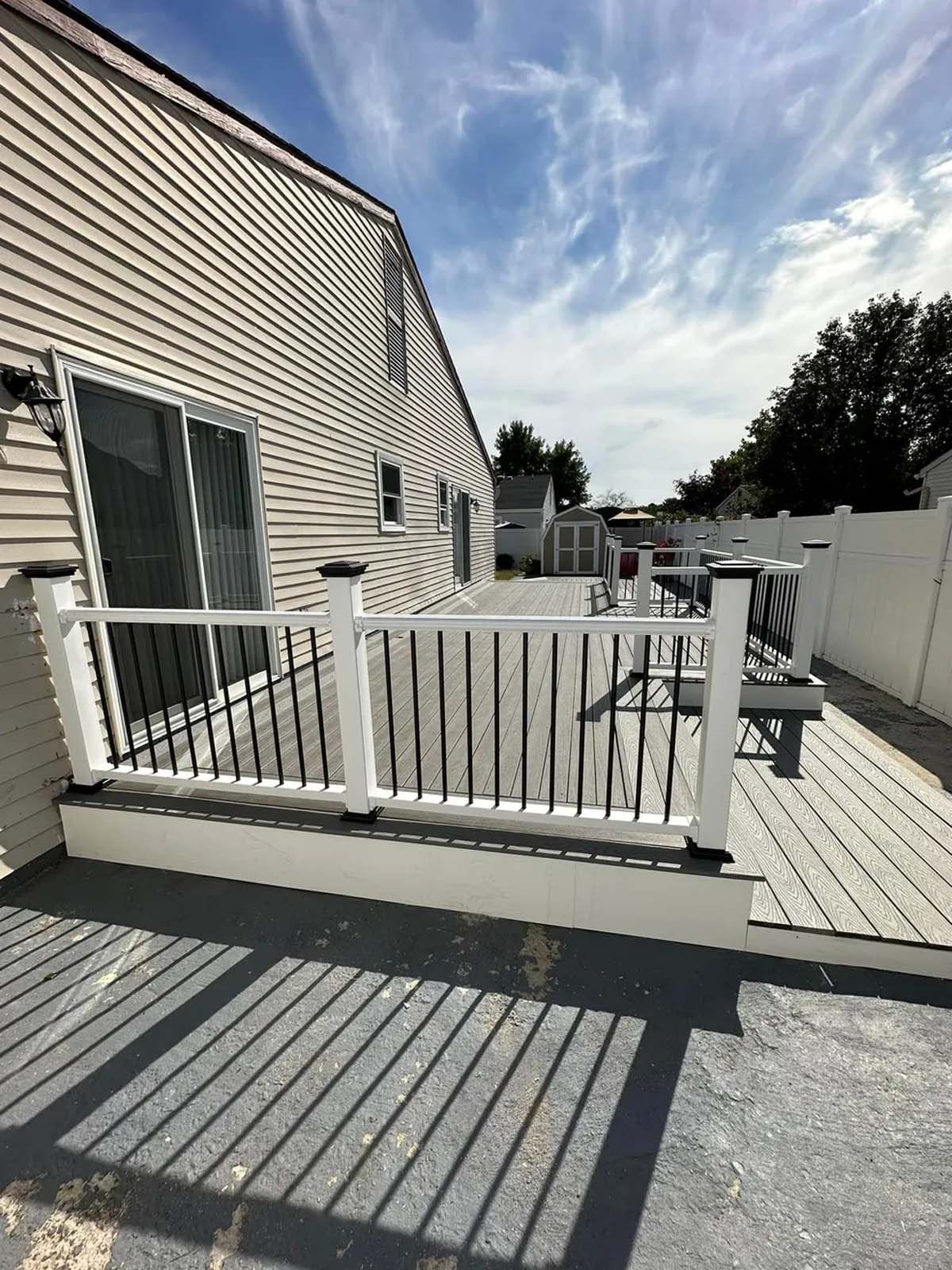 A large deck with a white railing is in front of a house.