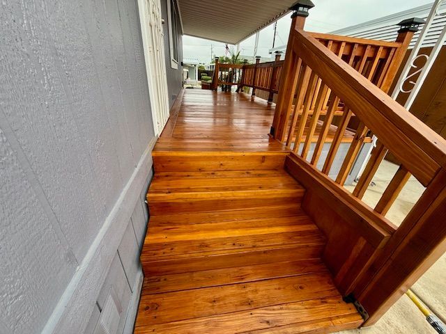 Wooden steps and deck leading to a house with gray siding. Handrails are visible.