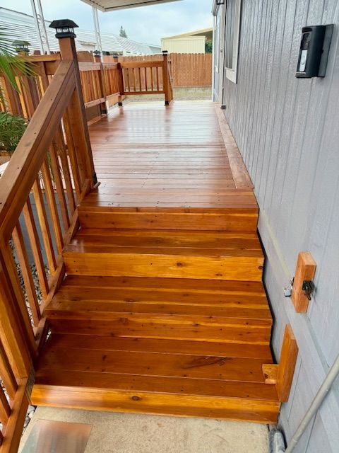 Wooden deck and stairs leading to a light-colored house. Brown stained wood, wet appearance.