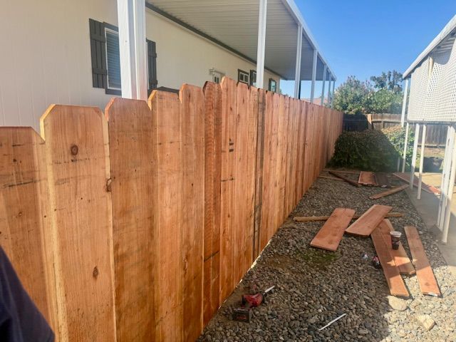 A wooden picket fence, newly built, extends along the side of a house.