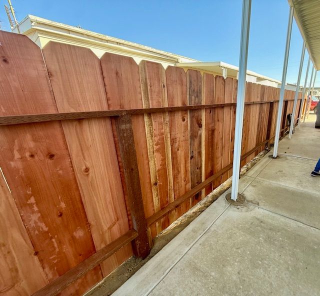 Wooden privacy fence along a cement walkway next to a building.